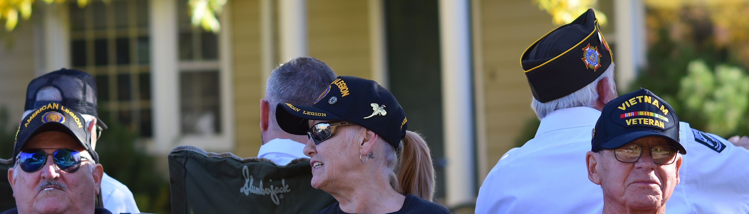 Older veterans in American Legion, VFW and Vietnam Veteran caps gathered at a community parade